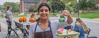 Person holding a decorated pumpkin at an outdoor pumpkin-painting activity.